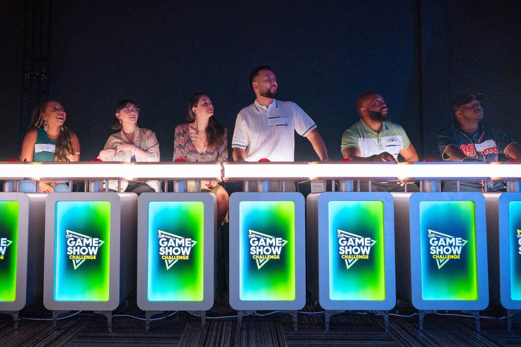 Contestants at glowing podiums during a live game show experience at The Game Show Challenge
