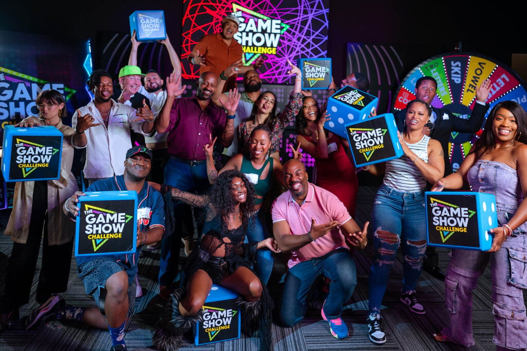 A large group poses with Game Show Challenge-branded giant dice. 