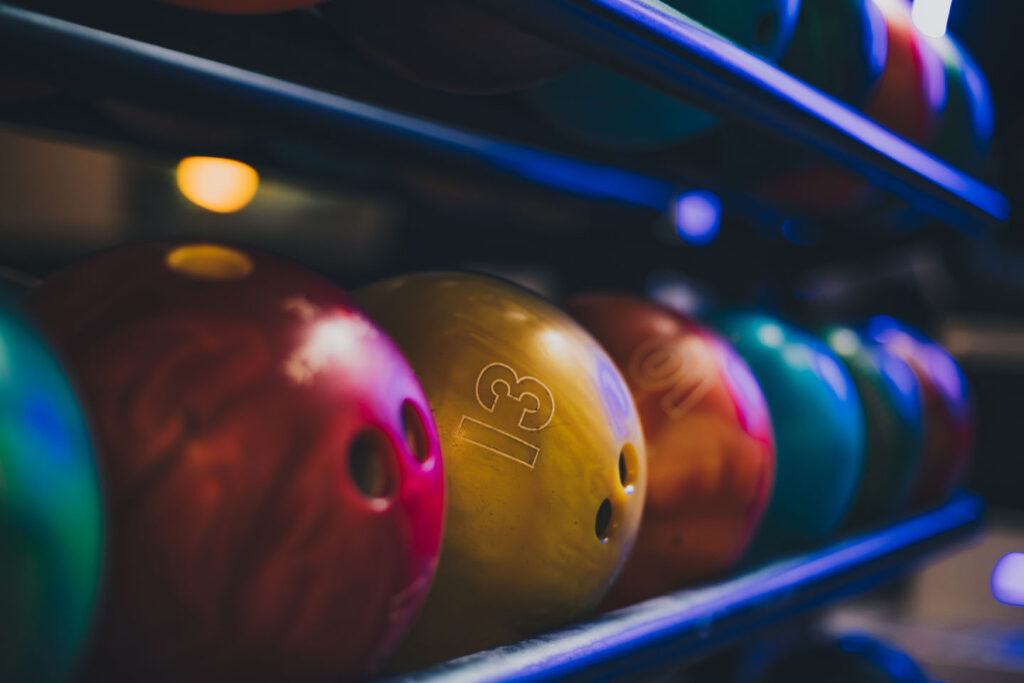 Rows of colorful bowling balls lit by blue neon light on a rack at a Greenville entertainment venue