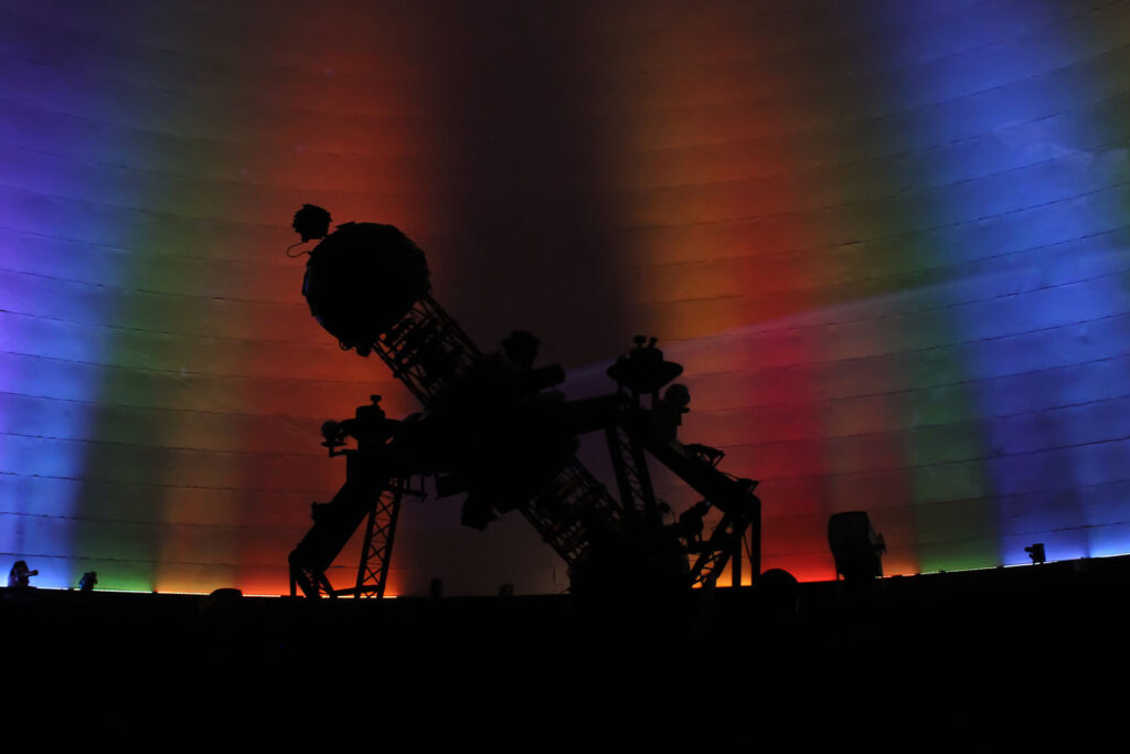 Silhouette of a large observatory telescope against a rainbow-lit planetarium dome, evoking Roper Mountain Science Center's T.C. Hooper Planetarium
